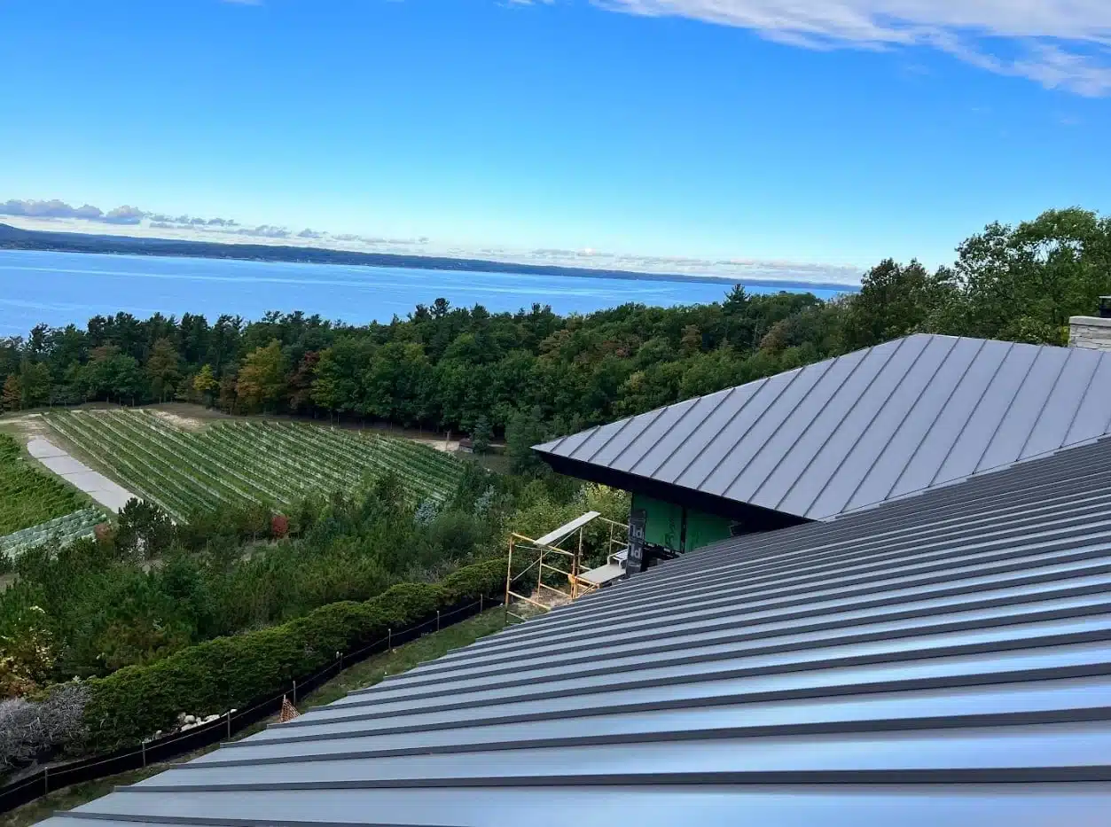 Metal rooftops overlook a vineyard and a body of water, with a line of trees on a clear day.
