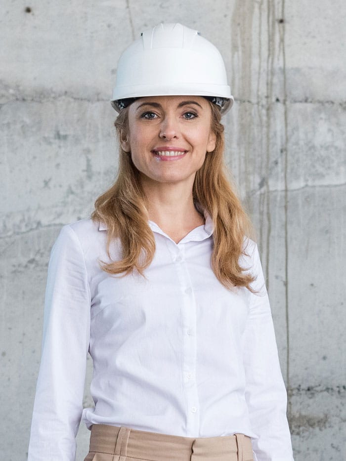 Person wearing a white hard hat and a white shirt, standing in front of a concrete wall.