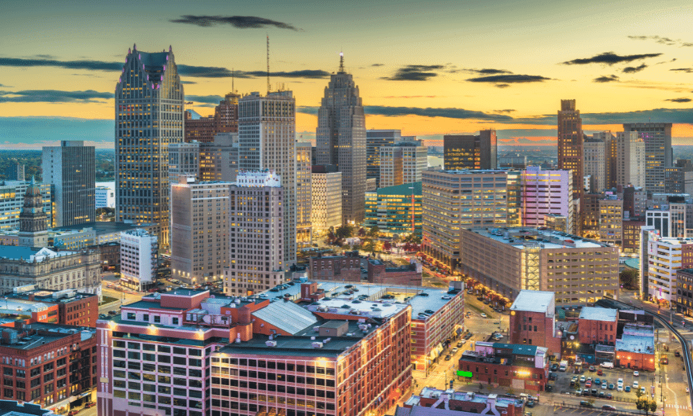 Aerial view of a cityscape at sunset with tall buildings, a mix of modern and historic architecture, and streets lined with lights.