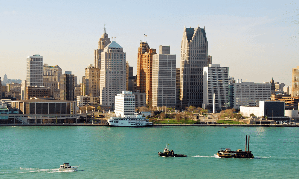 Skyline of a city with modern and historic buildings by a waterfront. A river has small boats and ships moving across the water.