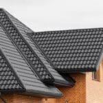 Close-up view of houses with orange brick walls and dark gray metal roofs under a cloudy sky.